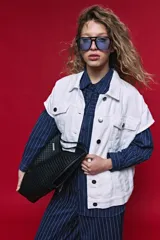 Chaleco de jean color blanco, de corte oversized, con cuello camisero, bolsillos delanteros con solapa y cierre frontal por botones metálicos.
