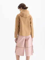Chaqueta color camel con capucha, cierre frontal y bolsillos laterales. Presenta un diseño de corte recto y forro interior a cuadros, con detalle de bordado en el pecho.