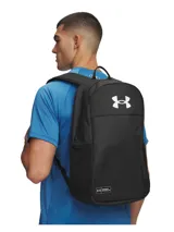 Mochila Under Armour color negro, con diseño clásico de cierre superior, bolsillo frontal vertical con cierre, bolsillos laterales de red y logo blanco estampado en la parte superior.