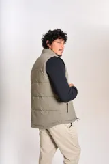 Chaleco puffer de corte regular, color beige, con cierre frontal y cuello alto. Presenta un diseño acolchado horizontal y logo bordado en el pecho.