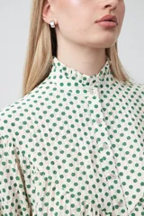 Camisa de viscosa con estampado de lunares, cuello alto con volados y cierre frontal de botones. Presenta un diseño de silueta suelta con frunces que aportan volumen y mangas largas con puños ajustados.