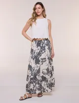 Falda maxi color crudo con estampado floral en tonos oscuros, tiro alto con cintura elástica fruncida, cordón de ajuste frontal y diseño escalonado de tres paneles con vuelo.