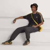 Camiseta de fútbol Adidas del Manchester United, modelo Terrace Icons. Diseño negro con sutiles rayas verticales moradas, franjas amarillas en los hombros y detalles bordados en dorado, incluyendo el trébol de Adidas y el escudo clásico del club.