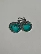 Aros colgantes con forma circular, hechos de resina color lila y borde de strass plateado. El aro es de acero quirúrgico plateado.