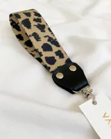 Llavero de tela con estampado animal print, detalles en cuero sintético negro y mosquetón metálico plateado.