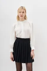 Falda corta negra plisada, de tiro alto con pretina ancha.