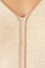 Suéter de punto color crema con cuello en V, mangas tres cuartos y detalle de costura vertical central. Presenta un diseño holgado con terminaciones acanaladas en puños y ruedo.