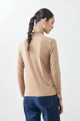 Remera de punto color tostado melange, con cuello alto con volados y mangas largas.