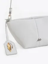 Bandolera de cuero vacuno con silueta estructurada, cierre superior y aplique metálico frontal. Incluye correa regulable y tag colgante con detalle decorativo.