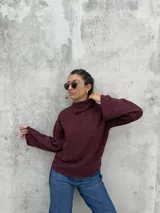 Polera de punto color bordó, con cuello alto abierto lateralmente, mangas largas amplias y corte recto.