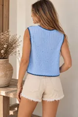 Chaleco de punto crochet color celeste, con bordados florales en tonos azules y blancos, escote en V y cierre frontal con botones. Cuenta con ribetes de terminación en azul oscuro.
