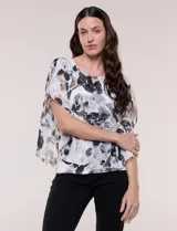 Blusa de gasa semitransparente con hilos de lúrex, diseño estampado floral en tonos blanco, gris y negro, silueta holgada tipo capa y escote redondo con detalle metálico.