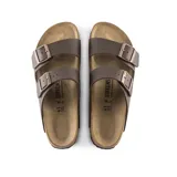 Sandalias Birkenstock modelo Arizona con dos correas ajustables con hebillas metálicas. Presentan una plantilla anatómica de corcho y ante, con suela de EVA y material superior Birko-Flor en color marrón oscuro.