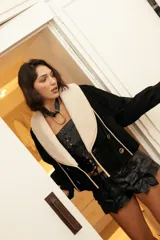 Chaqueta confeccionada en gamuza color negro con amplio cuello smoking de corderito en tono crudo. Presenta un diseño corto, cruzado con doble abotonadura y botones metálicos, mangas amplias y bolsillos.