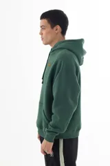 Buzo hoodie verde oscuro con corte oversize, confeccionado en algodón y poliéster. Estampa trasera de la Pantera Rosa como smuggler y logo bordado en el frente.