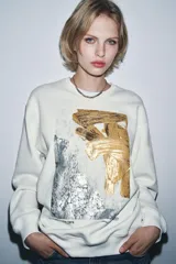 Sudadera de cuello redondo y manga larga, con diseño de estampado artístico metalizado en tonos dorados y plateados en el frente. Presenta acabados en rib en cuello, puños y ruedo.