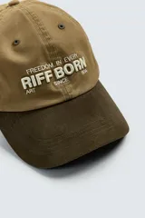 Gorra de seis paneles confeccionada en tejido de algodón con visera de efecto ante en contraste. Presenta un bordado frontal con el texto 'Freedom in every stiff born since 1934' y ajuste regulable en la parte posterior.