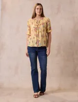 Blusa de gasa estampada con cuello a la base, escote en V plisado y lazo de ajuste. Delantera con detalles en puntilla y manga corta con puño fruncido.