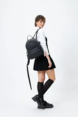 Mochila negra de símil cuero con acabado mate, diseño minimalista y bolsillo frontal con cierre metálico.