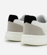 Championes urbanos blancos de material sintético con detalles en gris y negro. Presentan punta redonda, cordones, perforaciones para mayor respirabilidad y suela bold.