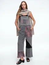 Mono de jean con diseño patchwork que combina diferentes texturas y estampados, incluyendo animal print y motivos geométricos. Presenta corte recto, bolsillos frontales y terminaciones deshilachadas.