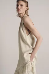 Top halter color crudo, de escote en V y diseño confeccionado en hilatura con mezcla de viscosa. Presenta bajo asimétrico con flecos al tono y cierre en la espalda.
