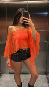Top tipo capa de tul translúcido en color naranja neón, con diseño asimétrico de hombros caídos y mangas amplias tipo murciélago.