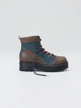 Bota de estilo trekking con diseño multicolor en tonos marrón, azul y detalles en rojo. Presenta plataforma de goma dentada, cordones tipo cuerda de escalada y cuello acolchado.