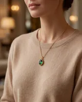 Collar de cadena fina dorada con dije ovalado de piedra verde esmeralda en marco de bronce.