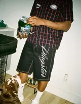 Conjunto compuesto por una camisa de manga corta a cuadros rojos y negros con detalles gráficos bordados y un short negro de corte holgado con costuras en contraste y estampa lateral con tipografía cursiva.