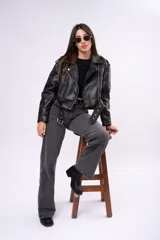 Campera biker de cuero sintético negro con cierre asimétrico, solapas anchas, bolsillos con cierre y cinturón ajustable en la cintura con hebilla metálica.