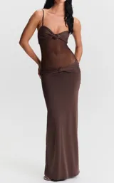 Vestido largo color marrón de silueta entallada, con tirantes finos, escote pronunciado con detalle de nudo y sección translúcida en la zona del torso con malla transparente.