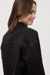 Sobrecamisa de denim negro con calce relajado, mangas largas, cuello clásico, cierre frontal con botones y bolsillo aplicado. Cuenta con detalles de strass en toda la prenda y terminación desflecada en el bajo.