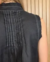 Musculosa marrón sin mangas, con cuello alto, escote en V y detalles de pespuntes blancos en contraste. Presenta pliegues y alforzas frontales.