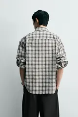 Camisa relaxed fit confeccionada en tejido de mezcla de algodón con textura irregular, diseño a cuadros en tonos gris, marrón y blanco, con cuello solapa, manga larga con puño abotonado, bolsillo de parche en el pecho y cierre frontal con botones.