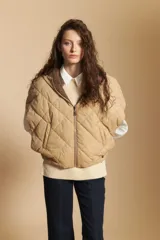 Chaleco de nylon matelaseado color beige, con diseño acolchado de rombos, cierre frontal y corte amplio tipo capa.
