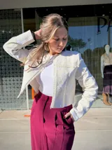 Chaqueta corta de estilo estructurado en color beige, con diseño de brocado floral en relieve y terminaciones desflecadas en el frente y cuello. Presenta mangas largas y cierre frontal oculto.