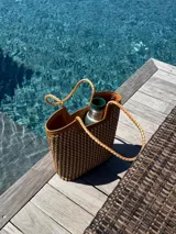 Bolso tipo tote bag de cuero trenzado a mano, en tonos marrón y negro, con asas trenzadas.