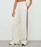 Pantalón deportivo de corte oversized estilo college, confeccionado en microfibra color crema con rayas laterales contrastantes en color marrón. Presenta cintura fija, bolsillos funcionales y frisos frontales.