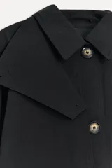 Trench negro de algodón con cuello solapa, manga larga con puños, solapa con trabilla y botón en el cuello, bolsillos laterales, cinturón de lazo en el mismo tejido, bajo con abertura en la espalda y cierre frontal con botones.