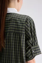 Vestido camisero midi de calce relajado a cuadros en tonos verde y negro, confeccionado en algodón liviano. Presenta cuello clásico en contraste de color blanco, cartera frontal oculta con botones y mangas cortas con vuelta.