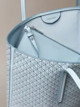 Cartera tote pequeña y estructurada de Calvin Klein en color celeste, con estampado integral de monograma CK. Incluye asas de mano dobles y una cartera mini interior a juego con cierre superior.