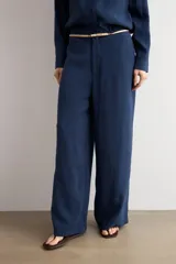Pantalón de corte recto y tiro medio, confeccionado en tejido negro de textura sutil. Presenta un diseño minimalista con cierre frontal oculto y caída fluida.