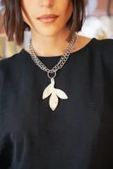 Collar de cadena de eslabones plateados con dije colgante de alpaca en forma de hoja con textura irregular. El diseño permite múltiples formas de uso.
