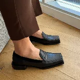 Mocasines negros de cuero con textura tipo reptil, punta cuadrada y detalle de aplique de cuero liso en el empeine.