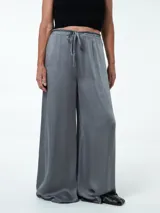 Pantalón gris de tela satinada, corte palazzo y cintura alta con cordón ajustable.