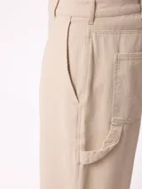 Pantalon recto de lona, color beige, con diseño de paneles reforzados en las piernas y cierre frontal con boton.