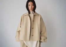 Chaqueta corta de algodón color beige, de corte holgado, con cuello clásico, cierre frontal de botones y bolsillos ribeteados. Cuenta con mangas largas amplias con puños ajustables mediante tiras y botones.