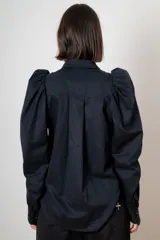 Camisa de algodón color marrón con mangas largas abullonadas, cuello clásico y cierre frontal oculto. Presenta botones decorativos con strass en los puños y en el cuello.