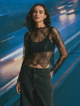 Top de encaje negro con diseño floral, manga larga y cuello redondo. Presenta un acabado festoneado en el ruedo y mangas.